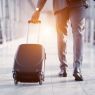 The photo presents a man at the airport, who's going for his trip in front of the rising sun. He holds a black suitcase in his left hand.